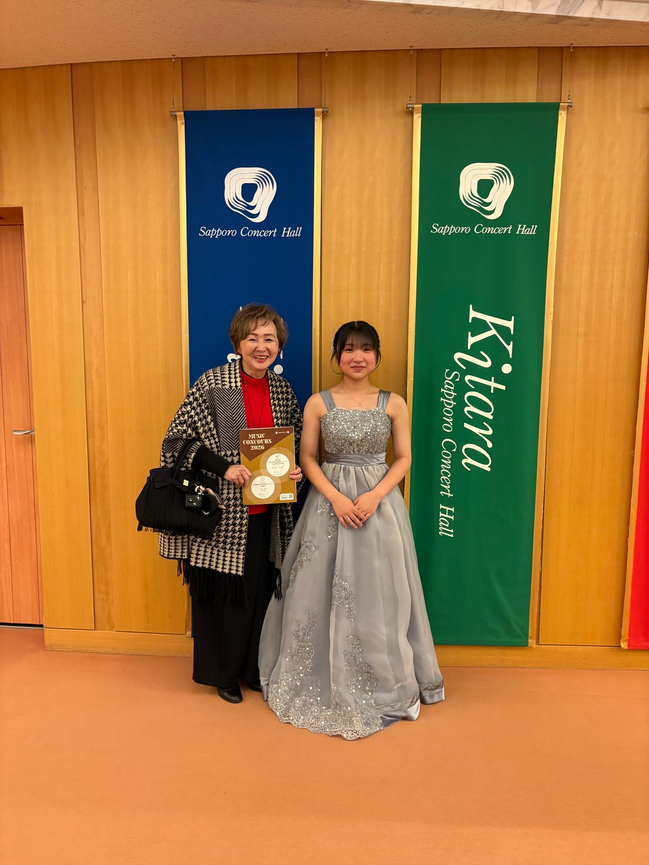 Kitaraのホール名を背景に演奏会用のドレス姿のSちゃんと楠雅子が並んだ記念写真